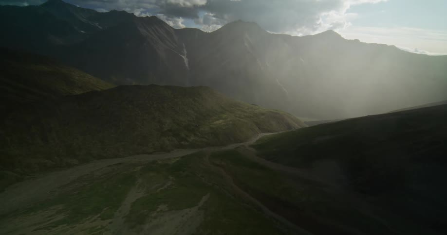 A majestic aerial view of a dramatic, sun-drenched mountain valley, with light rays piercing through hazy clouds