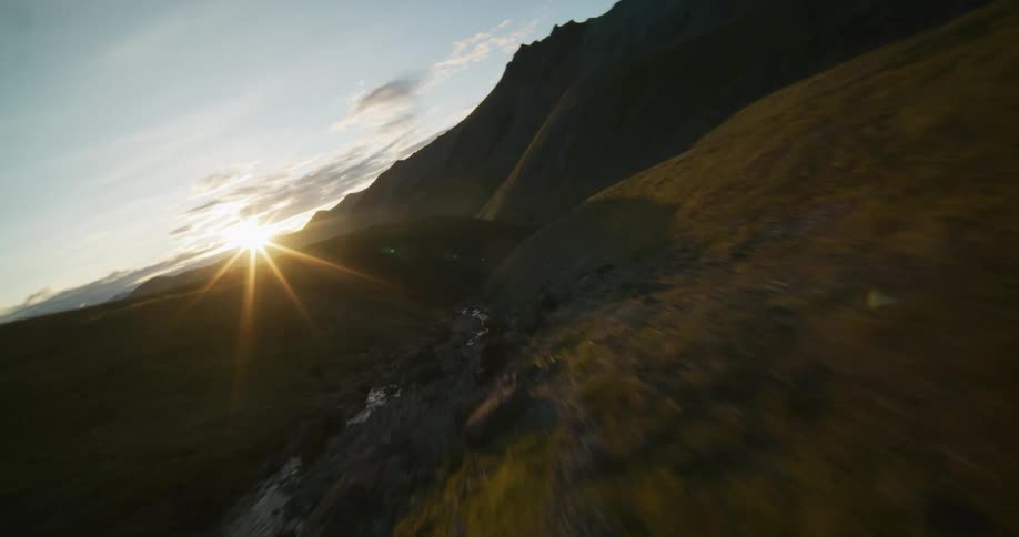An epic aerial view soars through a stunning mountain valley, following a riverbed as the golden sun sets