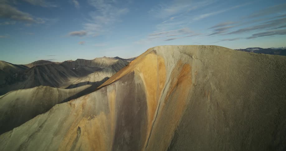 Epic aerial shot slowly reveals a vast, desolate mountain range with colorful mineral deposits at golden hour