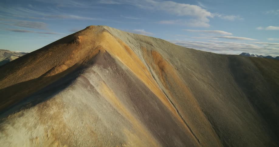 An epic aerial ascent over a colorful, mineral-rich mountain ridge reveals a breathtaking view of the vast mountain range beyond