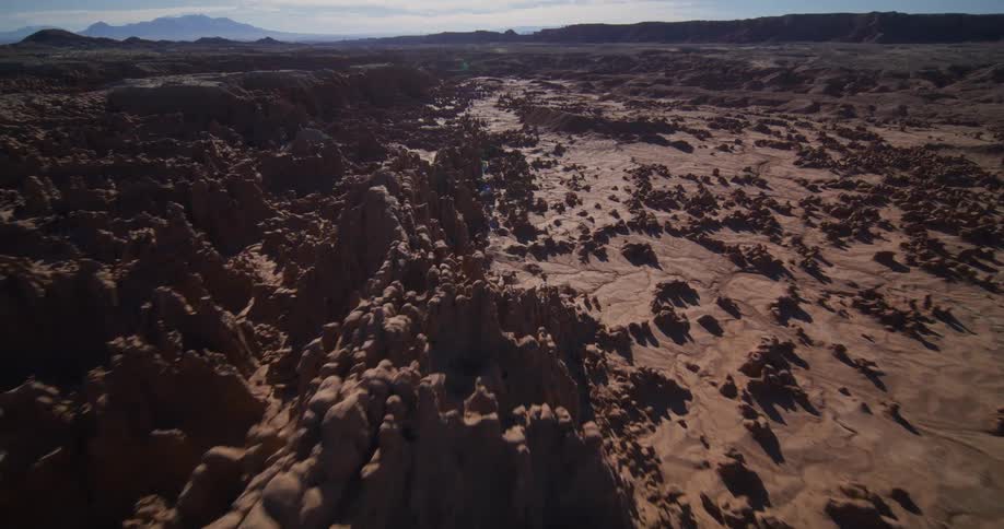 Slow aerial pullback reveals the vast and otherworldly landscape of a sun-drenched desert badlands with unique rock formations