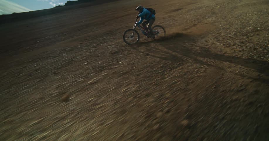 Slow motion tracking shot of an extreme mountain biker speeding down a steep, loose gravel hill