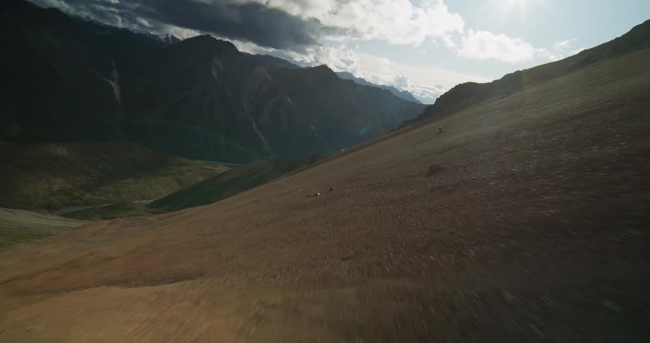 An adventurous mountain biker expertly navigates a treacherous descent down a vast, sun-drenched mountain scree slope