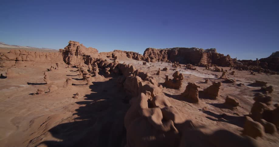 An FPV drone soars low and fast over the unique hoodoo rock formations of a surreal desert landscape under a clear blue sky