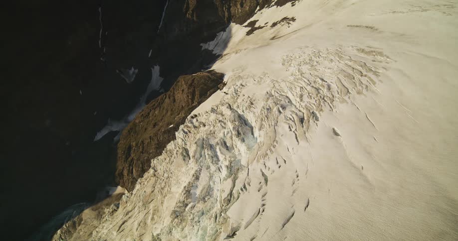 An immersive aerial journey through thick clouds reveals a magnificent sun-kissed glacier nestled in a rugged mountain range
