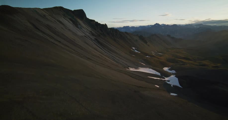 An epic aerial pullback reveals a vast and desolate mountain valley with snow patches at sunset