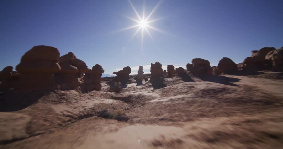 A smooth tracking shot glides through unique hoodoo rock formations in a desert valley under a bright sun