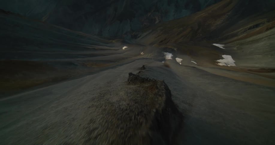 A first-person view aerial shot descends rapidly along a desolate and rugged mountain range during a golden sunset