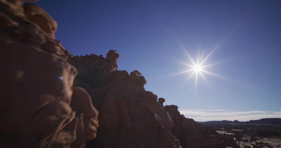A stunning aerial view pulls back over unique hoodoo rock formations, revealing a vast desert valley under a bright sunburst