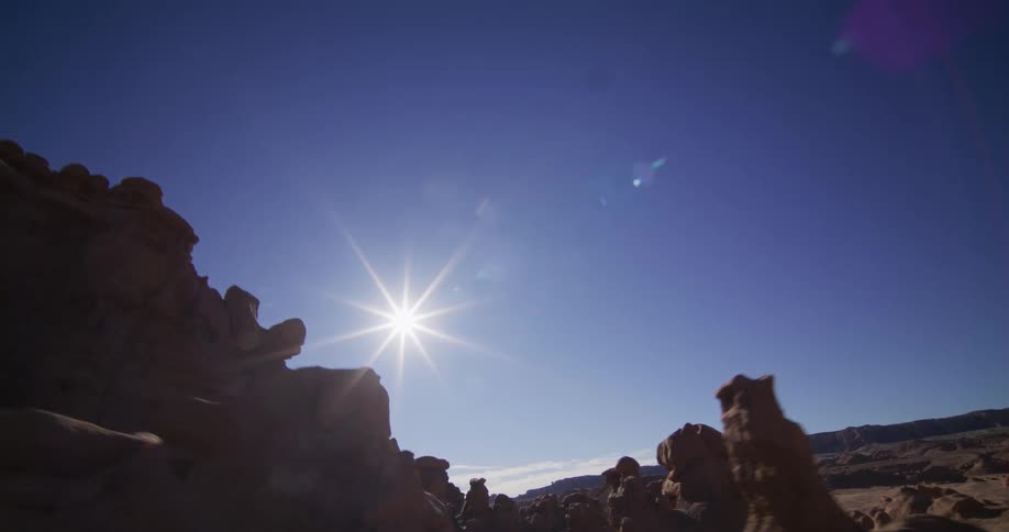 A cinematic tracking shot reveals a vast desert canyon filled with unique rock formations under a bright sun