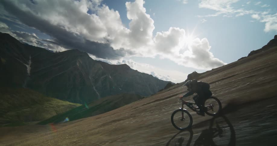 In dramatic slow motion, a mountain biker expertly shreds down a steep, rugged mountainside against a stunning sky