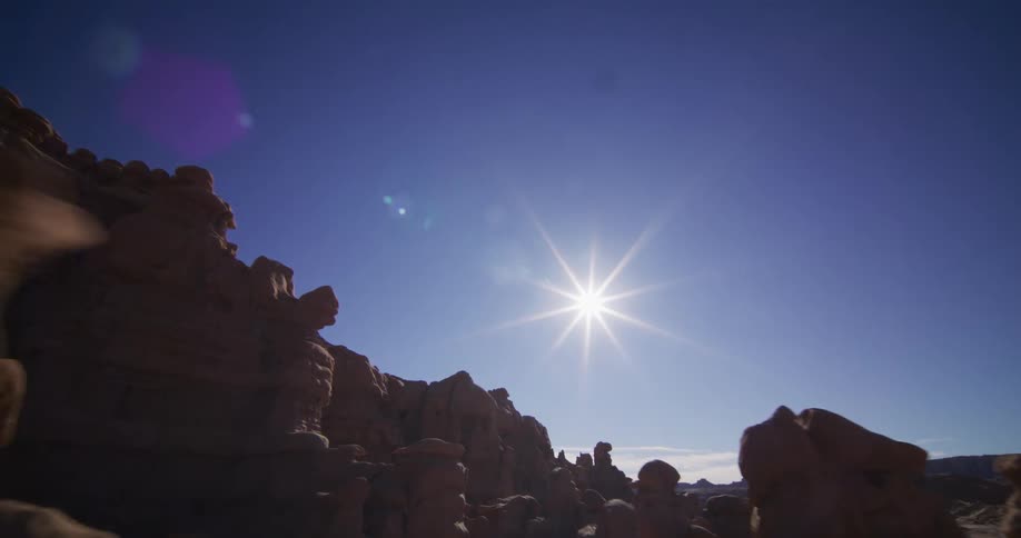 The bright sun shines over unique hoodoo rock formations in a vast desert canyon as the camera slowly reveals the landscape