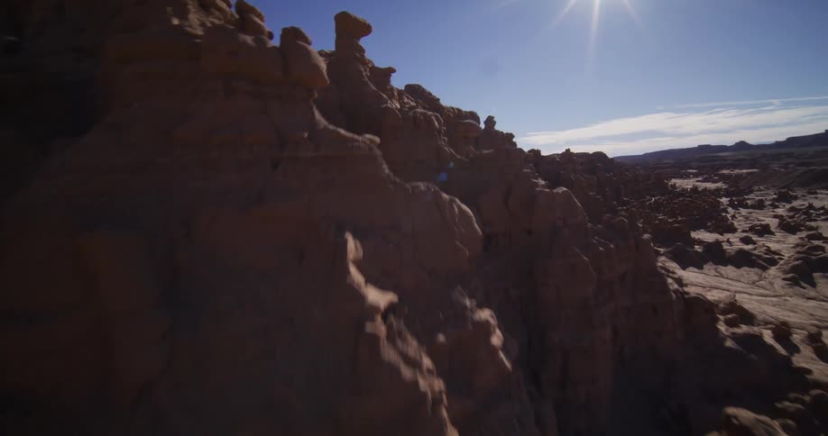 A soaring aerial shot flies over the surreal sandstone hoodoo formations of a desert valley on a bright, sunny day