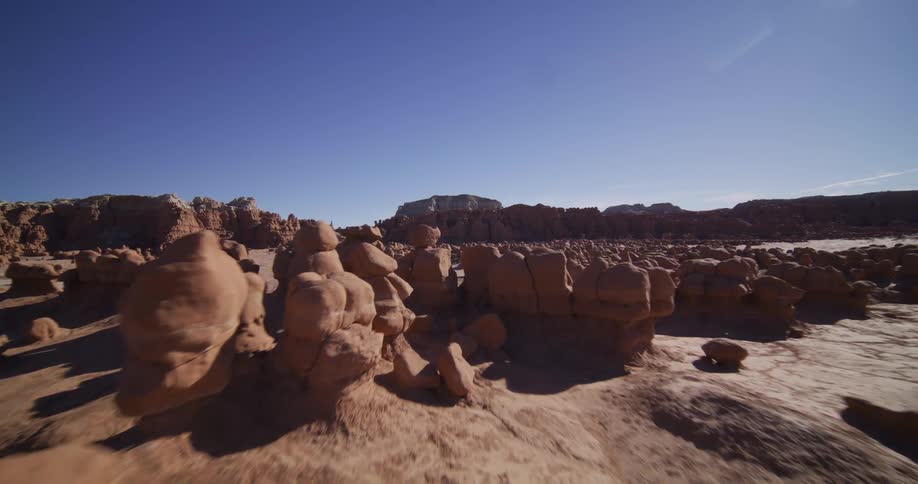 A low aerial tracking shot flies through the surreal, mushroom-shaped rock formations of Goblin Valley, Utah, on a bright, sunny day