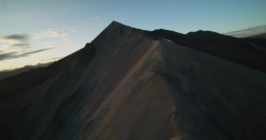 An epic aerial shot reveals the sun rising behind a dramatic and sharp mountain ridgeline
