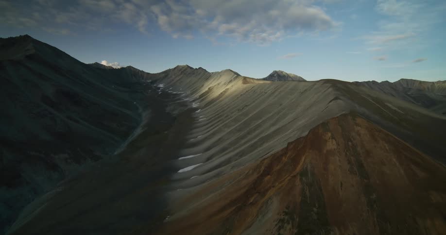 A slow aerial push reveals a majestic mountain range with peaks lit by the golden hour sun