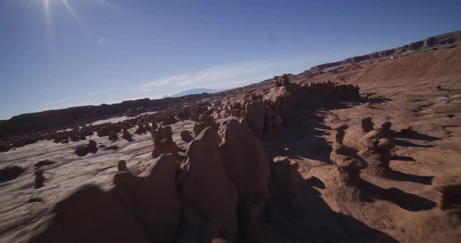 A breathtaking aerial FPV drone shot glides low over the unique goblin-like hoodoos in a sun-drenched desert landscape