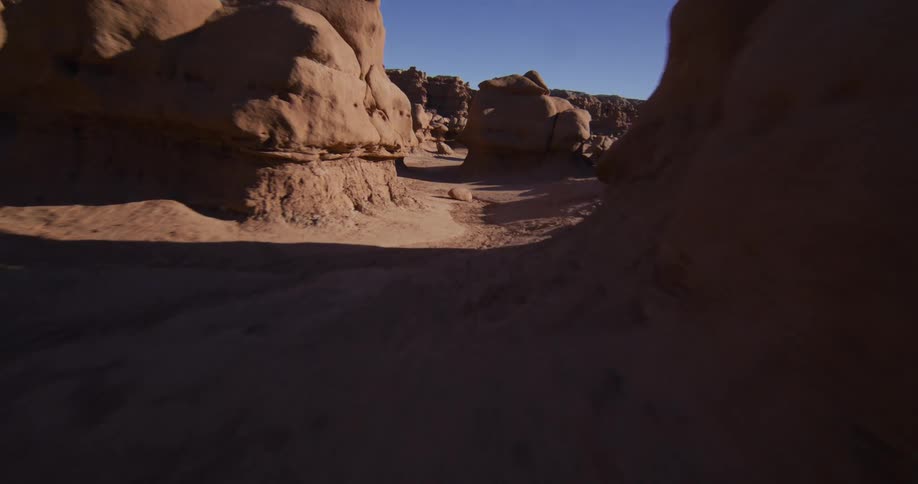 A smooth, low-flying aerial shot glides through the unique red rock hoodoo formations of Goblin Valley, Utah on a bright, sunny day