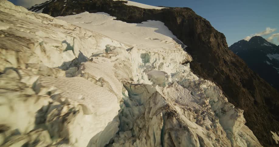 Dramatic aerial footage glides over the cracked and icy surface of a massive mountain glacier during golden hour