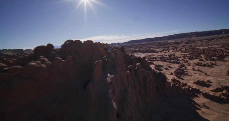 An epic aerial tracking shot flies over the unique hoodoo rock formations in a desolate desert valley on a sunny day