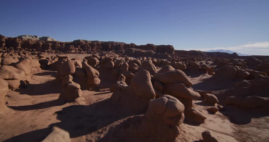 A stunning aerial journey glides through the surreal and otherworldly mushroom-shaped rock formations of a sunny desert valley