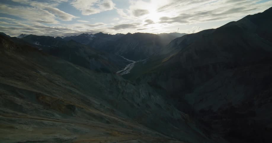 Majestic aerial shot pulling back to reveal a vast, shadowy mountain valley with a river winding through it at sunset