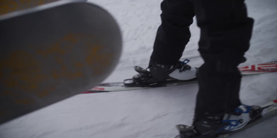 A detailed slow-motion shot of a skier's boots and skis moving across the snow at a resort