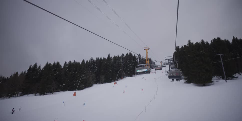 A point-of-view shot from a ski lift ascending a snowy mountain slope on a cloudy day