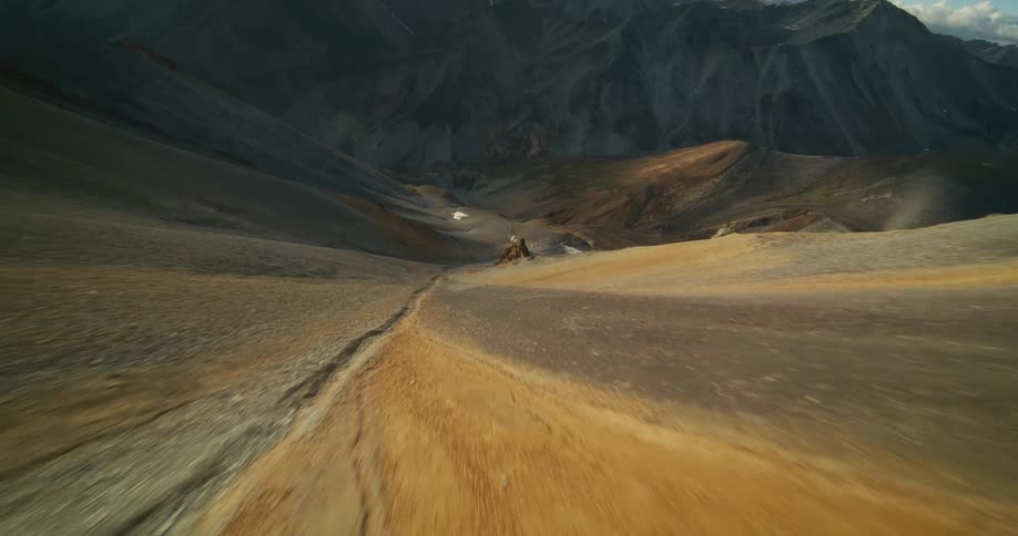 An epic aerial flight speeds over the barren, colorful ridges of a vast mountain range at sunset