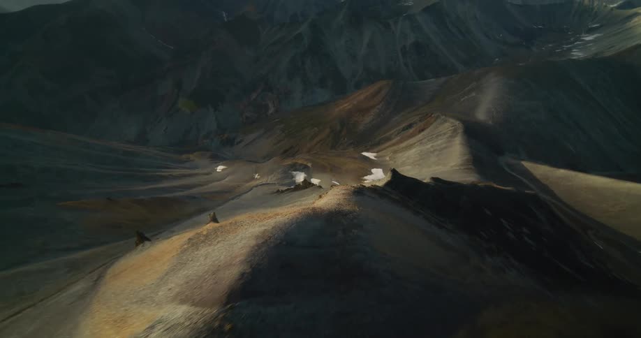 A cinematic aerial flight glides over the desolate, rocky ridges of a mountain range at golden hour