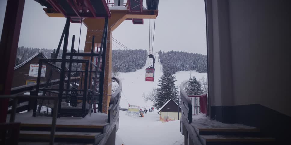 A lone red gondola ascends a snow-covered mountain at a ski resort under a gray winter sky