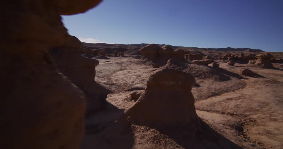 A smooth tracking shot explores the otherworldly sandstone hoodoos of a desert valley on a bright, sunny day