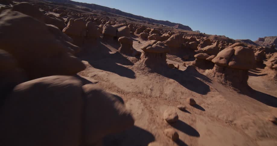 A slow and immersive aerial shot glides through the unique, mushroom-shaped rock formations of Goblin Valley on a sunny day