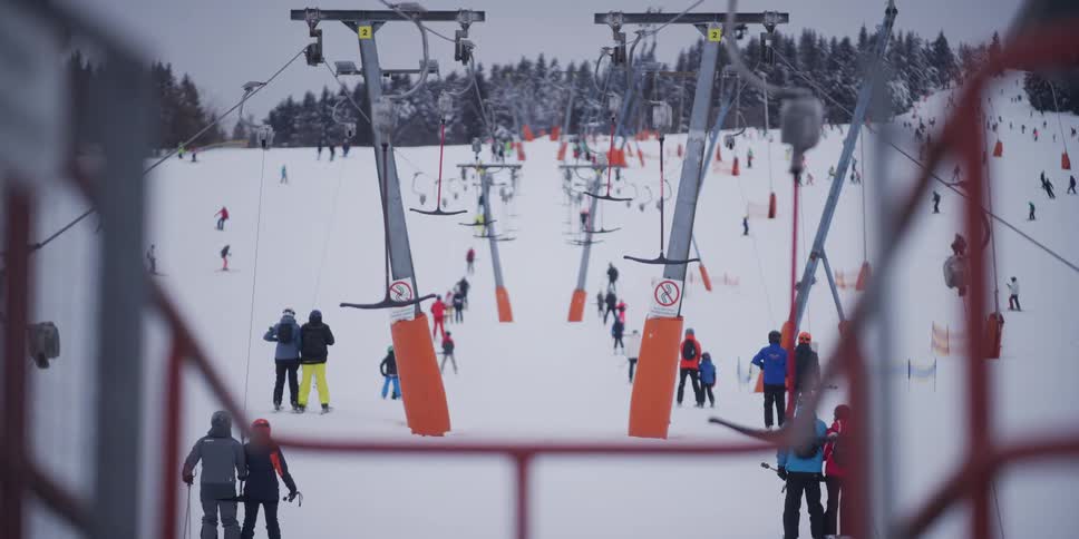 A bustling ski resort with skiers and snowboarders queuing for the T-bar lift on a snowy mountain