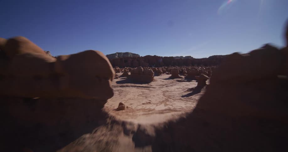 A smooth, low-angle tracking shot glides through the otherworldly landscape of Goblin Valley's unique rock formations under a bright sun