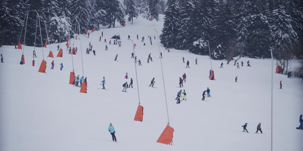 A bustling ski slope is filled with numerous skiers and snowboarders enjoying a winter day on the mountain in slow motion