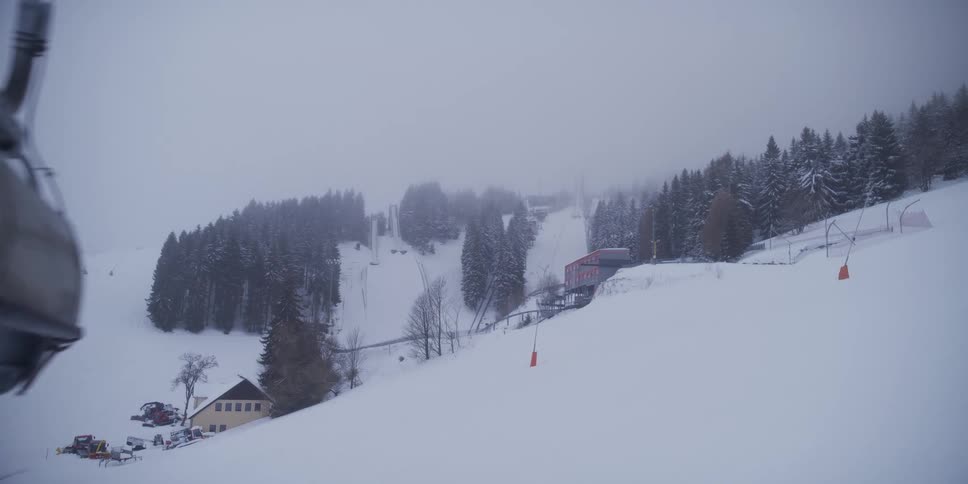 A ski lift chair passes over a snowy mountain slope at a resort on a foggy winter day