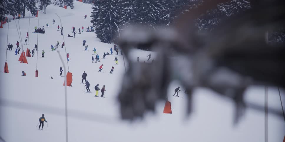 A distant view of many people skiing down a busy slope at a mountain ski resort on a winter day