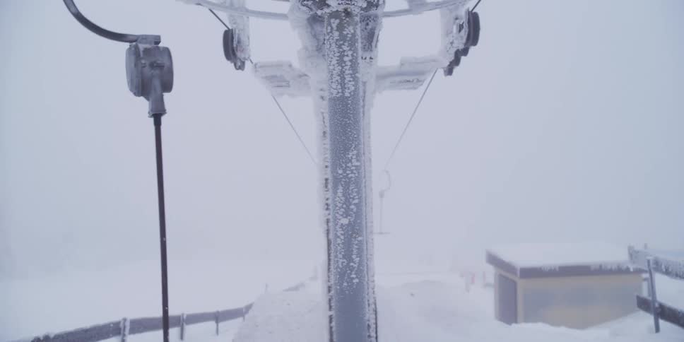 A close-up of a frost-covered T-bar lift mechanism moving slowly during a blizzard at a ski resort