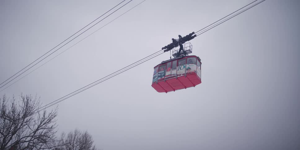 A bright red gondola lift travels across a bleak and overcast winter sky