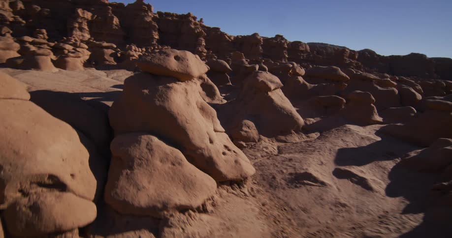 A slow, immersive journey through a valley of unique, weathered sandstone formations under a bright, clear desert sky