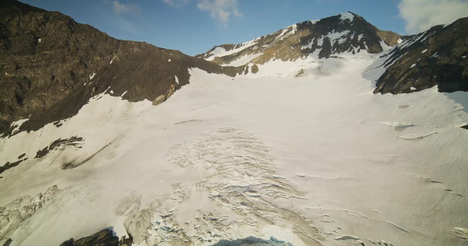 A majestic aerial view slowly reveals a vast glacier nestled between rugged mountain peaks under a clear blue sky