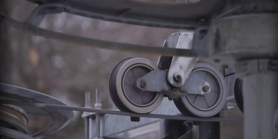 A close-up of a ski lift pulley system with wheels turning as the cable and t-bar pass through