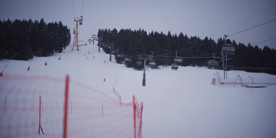 Skiers dot the snowy slope as a chairlift ascends the mountain on an overcast day