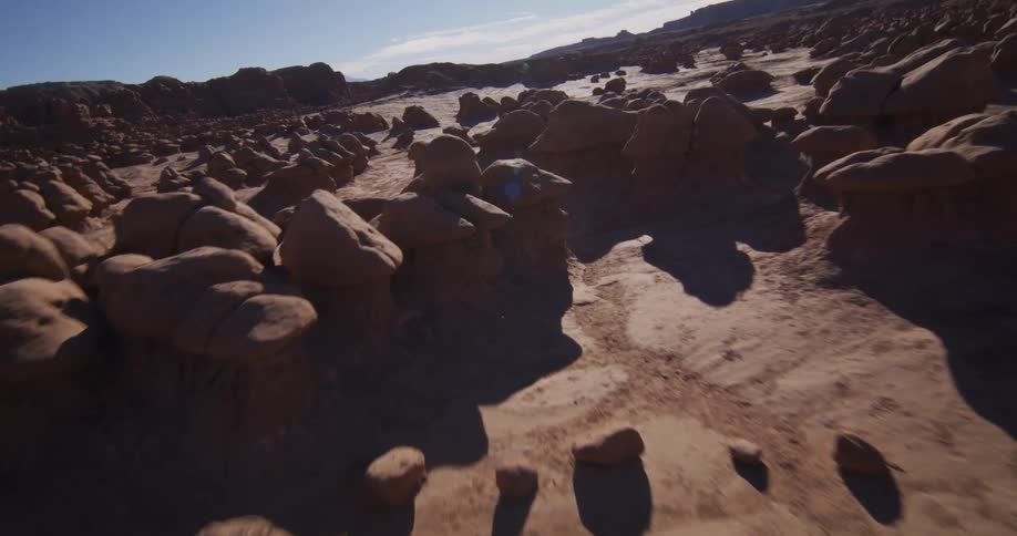 A low aerial flight weaves through the surreal hoodoo rock formations of a sun-drenched desert valley