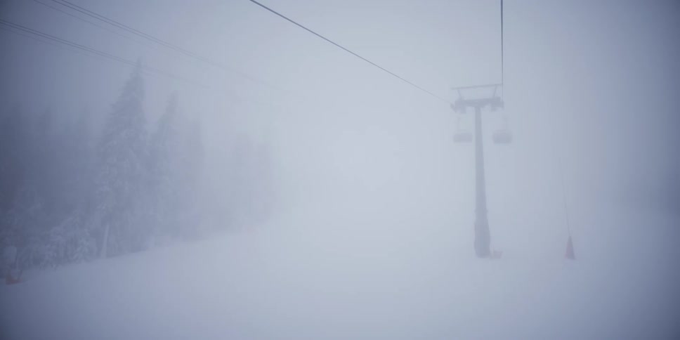 A solitary ski lift chair passes by and disappears into the thick white fog on a snowy mountainside