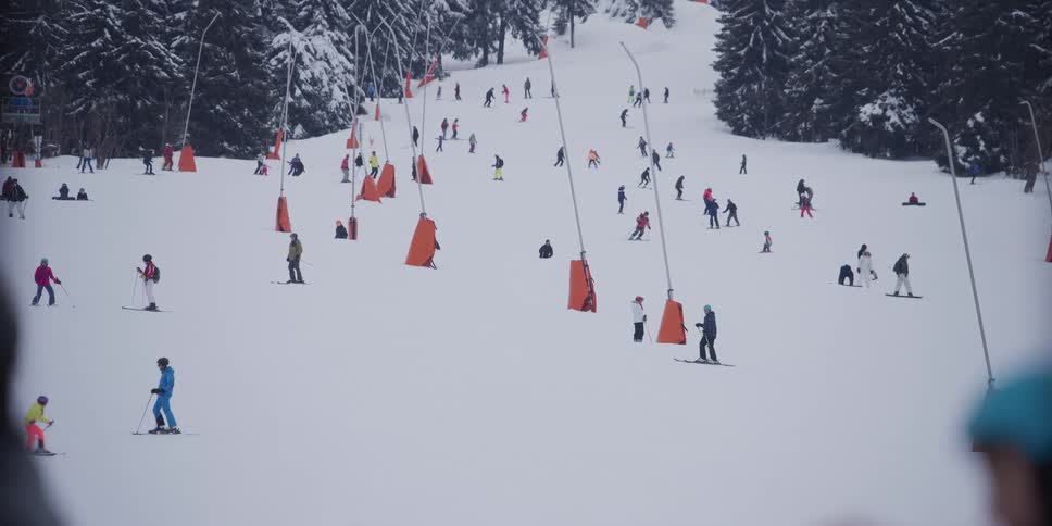 A bustling ski slope is filled with skiers and snowboarders enjoying a day on the snowy mountain surrounded by evergreen trees