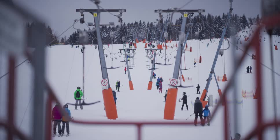 T-bar lifts carry skiers and snowboarders up a bustling snowy slope at a winter ski resort