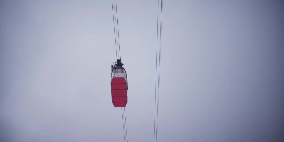 A lone red gondola slowly ascends into the sky, disappearing into the thick white fog on a winter day