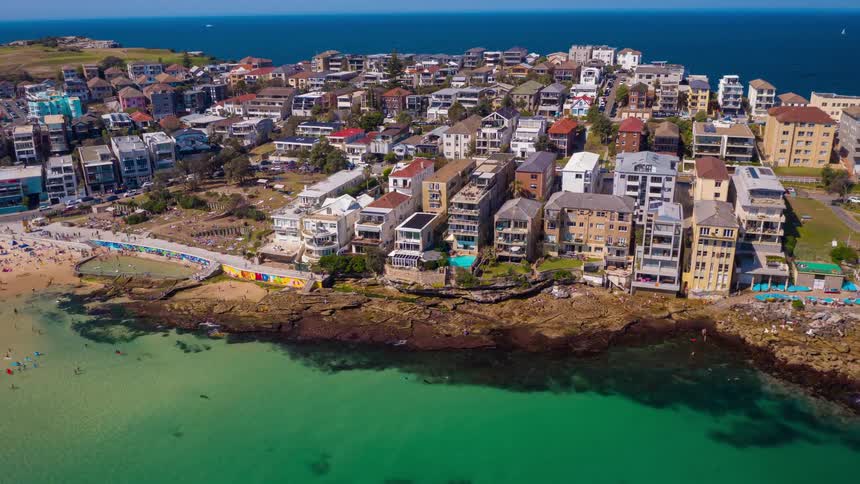 A beautiful orbiting aerial view of the iconic Bondi Beach in Sydney, Australia, bustling with people enjoying the sun on the golden sand and in the turquoise ocean